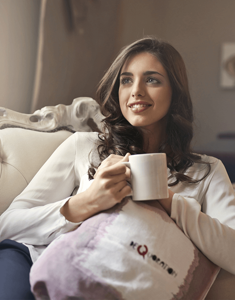 Frau sitzt glücklich mit Kaffeetasse auf der Couch